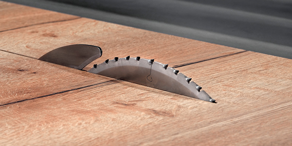 A picture of a diamond circular saw blade on a table top machine cutting wooden pannel